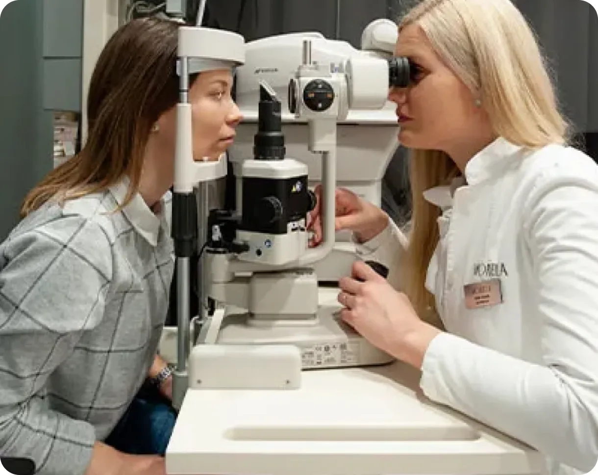 A clinician guiding a patient through an eye examination at a slit lamp.