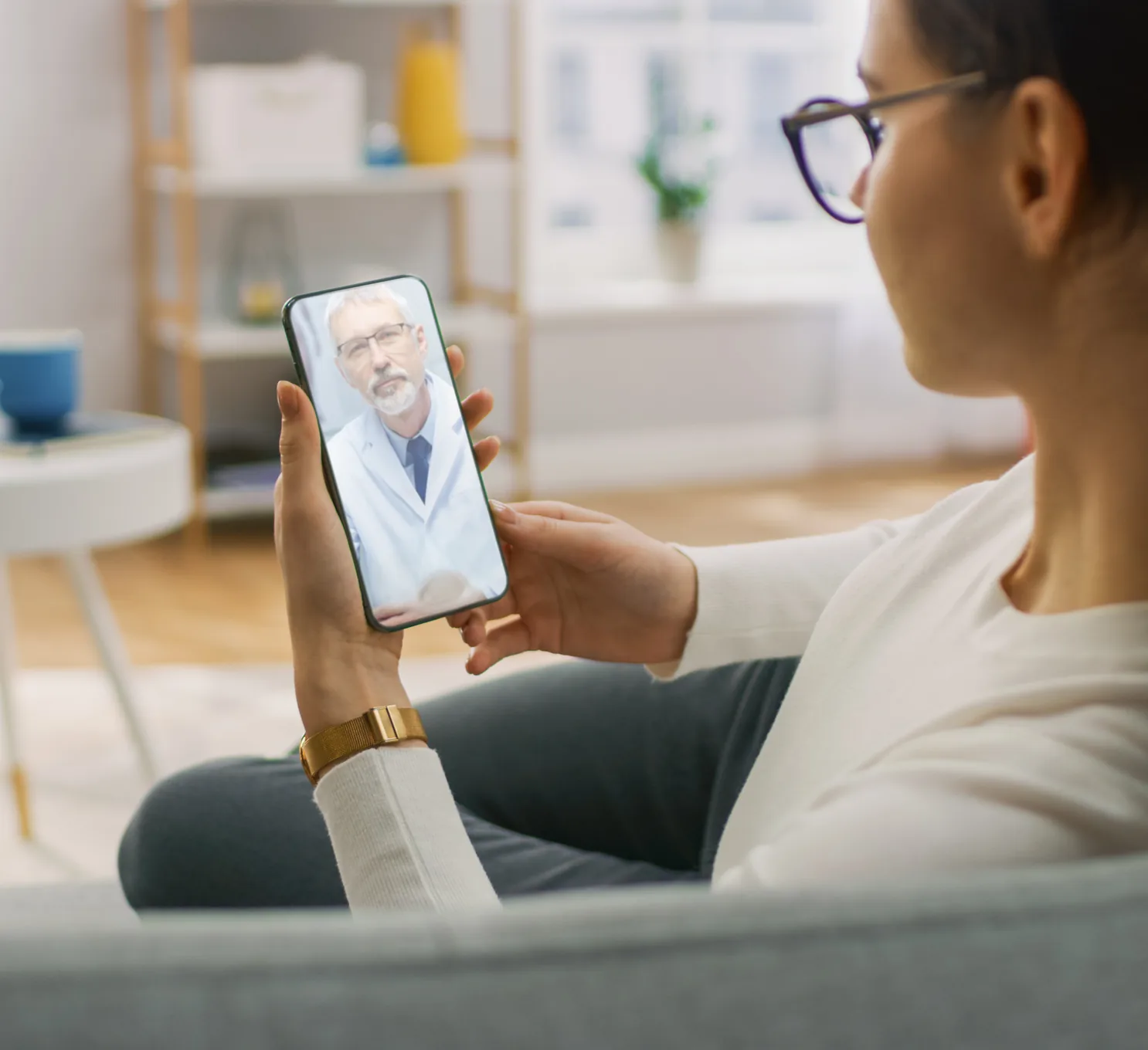 A patient on a video call with a clinician from her sofa at home.