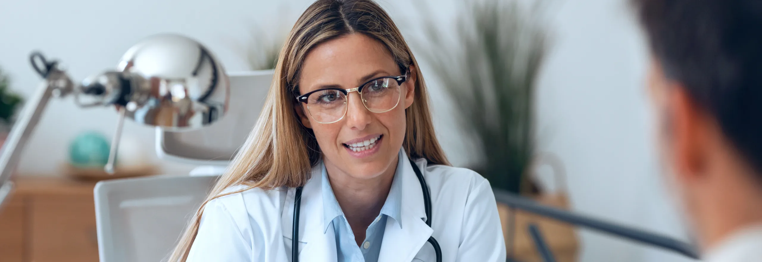 A clinician in conversation with a patient across a consulting-room desk.